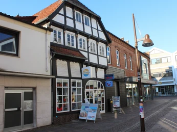 Fachwerkhaus in einer Einkaufsstraße mit Schaufenstern und Reisepostern zwischen modernen Gebäuden.