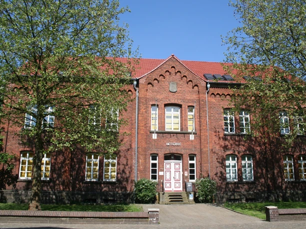 Backsteinfassade des Amtsgerichts Achim, flankiert von Bäumen unter blauem Himmel, Eingang mittig.