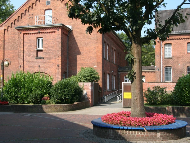 Backsteingebäude des Amtsgerichts Achim mit umgebendem grünen Garten und rotem Blütenbeet im Vordergrund.