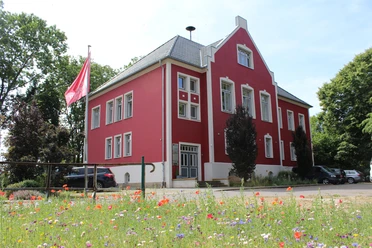 Amtshof 1 in Bruchhausen-Vilsen, ein rotes Gebäude mit weißen Fensterrahmen und Blumenwiese davor.