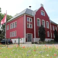 Amtshof 1 in Bruchhausen-Vilsen, ein rotes Gebäude mit weißen Fensterrahmen und Blumenwiese davor.
