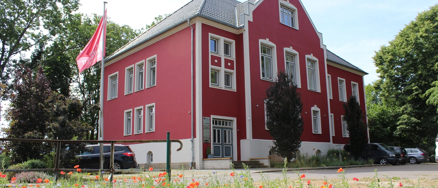 Amtshof 1 in Bruchhausen-Vilsen, ein rotes Gebäude mit weißen Fensterrahmen und Blumenwiese davor.