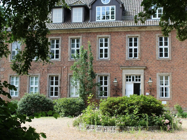 Ein rotes Backsteingebäude mit vielen Fenstern, umgeben von Grün, bildet den Amtshof in Bruchhausen-Vilsen.