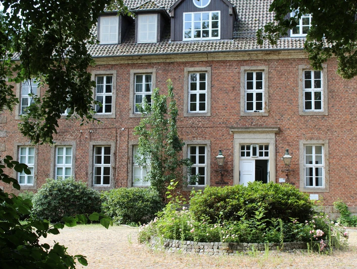 Ein rotes Backsteingebäude mit vielen Fenstern, umgeben von Grün, bildet den Amtshof in Bruchhausen-Vilsen.