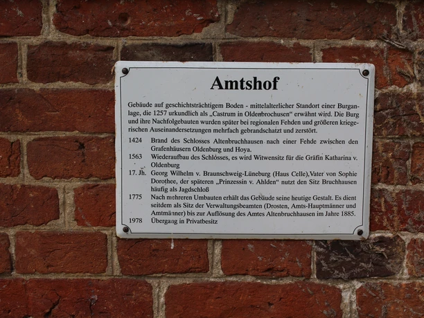 A metal information panel on the red brick wall of the Bruchhausen-Vilsen administrative compound explains historical details.