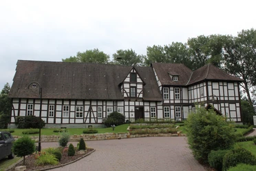 Fachwerkgebäude des Amtshofs Steyerberg mit gepflasterter Einfahrt und umgebenden Bäumen im Hintergrund.