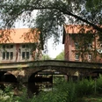 Die Aue-Brücke in Steyerberg, umgeben von Bäumen, verbindet historische Backsteingebäude über einen Fluss.
