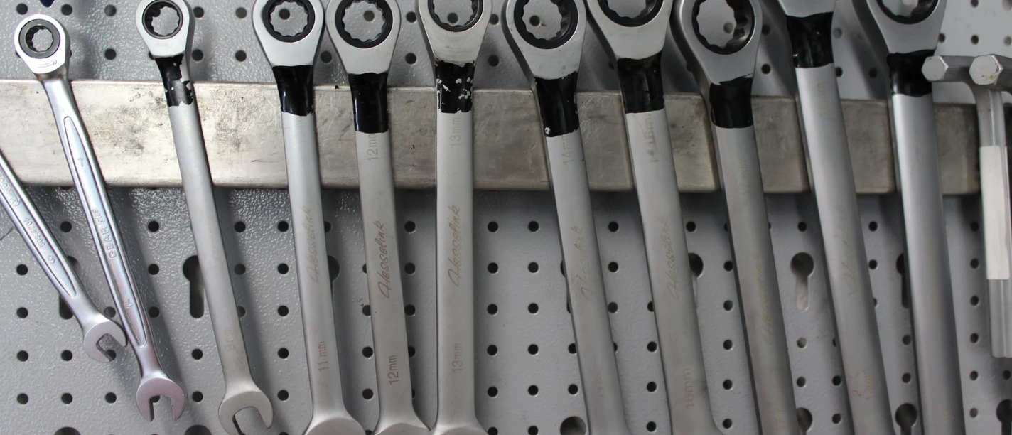 Eine Reihe von silbernen Ratschen-Ringschlüsseln hängt ordentlich auf einer Lochwand.