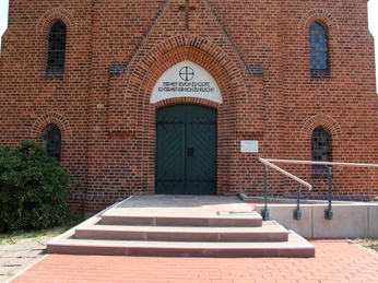 Kirche Bruchhausen Backsteinfassade der Kirche Bruchhausen mit grünen Türen und einladenden, barrierefreien Stufen.