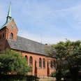 Backsteinkirche mit Spitzdach und Turm im Dorf Bruchhausen; von Bäumen umgeben, blauer Himmel.