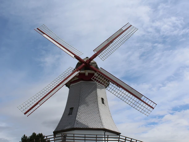The Behlmer Wedding Mill, with its white sails framed in red, against a blue sky in a rural setting.