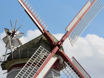 Historische Windmühle mit rot-weißen Flügeln vor blauem Himmel im Norden Deutschlands.
