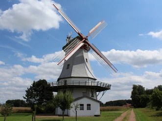 Eine historische Windmühle mit roten Flügeln vor blauem Himmel und eine ländliche Umgebung.