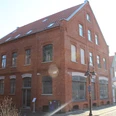 Historisches rotes Backsteingebäude mit spitzem Giebel, großen Fenstern und Straßenlaterne davor.