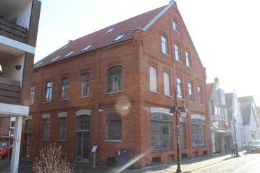 Biskuithaus Historisches rotes Backsteingebäude mit spitzem Giebel, großen Fenstern und Straßenlaterne davor.