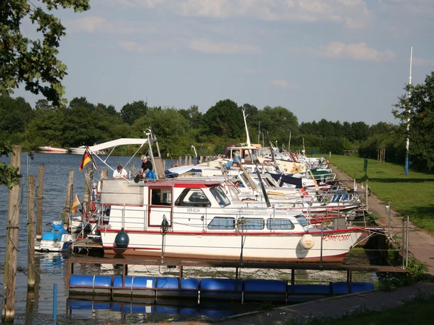 Am Weserufer in Mehlbergen liegen Motorboote vor grünen Wiesen und Bäumen vertaut am Steg.