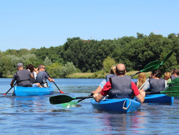 Kanutour Mittelweser Eine Gruppe von Menschen in blauen Kanus paddelt über einen ruhigen Fluss, umgeben von grünen Bäumen.