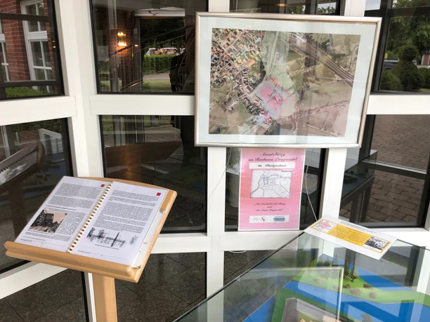 Burg Langwedel Im Eingangsbereich ein Luftbild der Burg Langwedel an der Wand und ein informatives Buch auf einem Ständer.