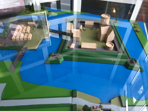 Modell der Burg Langwedel auf einer blau-grünen Fläche, mit modernen Strukturen und Wasser umgeben.