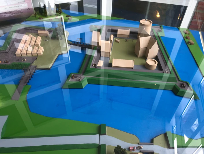 Modell der Burg Langwedel auf einer blau-grünen Fläche, mit modernen Strukturen und Wasser umgeben.