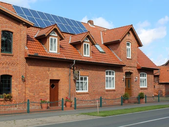 Ein rotes Backsteingebäude mit Solarpanels auf dem Dach und Fenstern, an einer Straßenkreuzung.