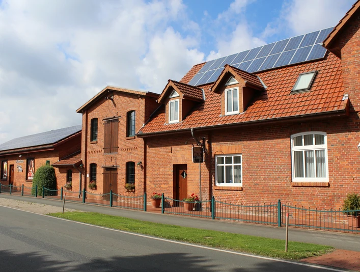 Alte, sanierte Mühle aus rotem Backstein mit modernen Solarpanelen auf einem idyllischen Dorfweg.