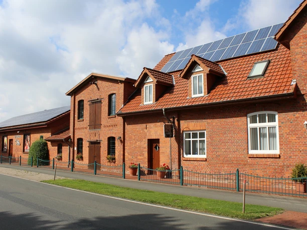 Buschens Mühle Nordholz Alte, sanierte Mühle aus rotem Backstein mit modernen Solarpanelen auf einem idyllischen Dorfweg.
