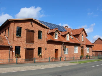 Historische Backsteinmühle mit modernen Solarpaneelen auf dem Dach in ländlicher Umgebung.