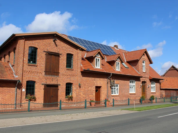 Historische Backsteinmühle mit modernen Solarpaneelen auf dem Dach in ländlicher Umgebung.