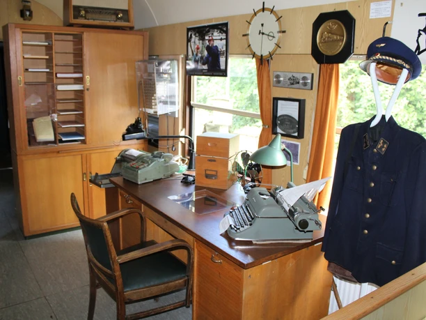 Museumslok Ausstellung A historic locomotive office with antique furniture, typewriter and uniform on a clothes rack.