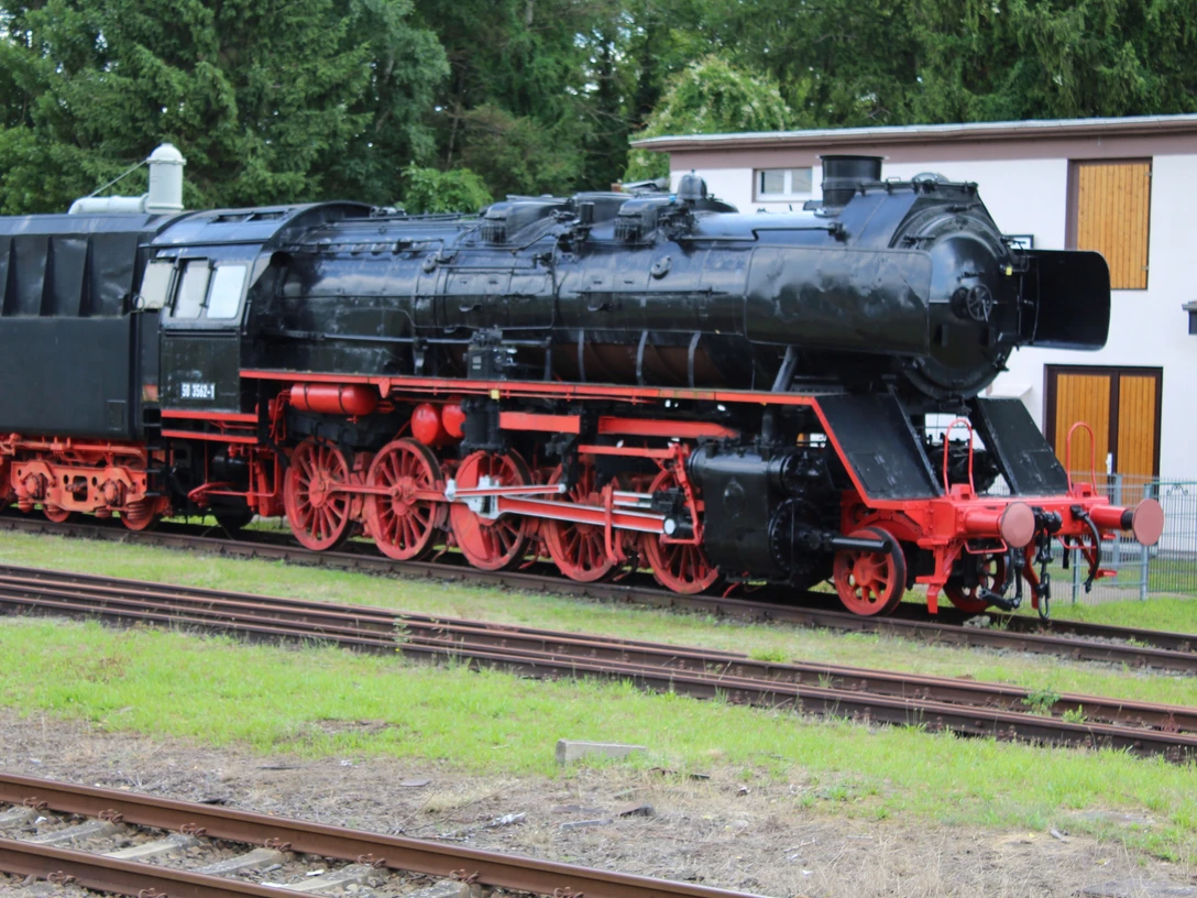 Weyhe Museumslok Historische Dampflok im Freien, schwarz mit roten Rädern, umgeben von Bäumen und einer Hütte.Historic steam locomotive outdoors, black with red wheels, surrounded by trees and a hut.Historisk damplokomotiv i det fri, sort med røde hjul, omgivet af træer og en hytte.Historische stoomlocomotief buiten, zwart met rode wielen, omringd door bomen en een hut.