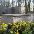 Gedenkstätte mit Blumen und Inschrift "Den Brüdern und Schwestern 1939-1945", umgeben von Bäumen.