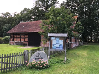 Ole Schüne Magelsen Ein historisches Backsteingebäude mit Holzfachwerk und einem steinernen Schild im Vordergrund.