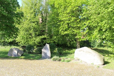 Partnerkommunen Drei Gedenksteine stehen auf einem gepflegten, sonnigen Platz, umgeben von üppigem Grün.