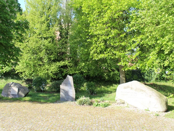 Partnerkommunen Drei Gedenksteine stehen auf einem gepflegten, sonnigen Platz, umgeben von üppigem Grün.