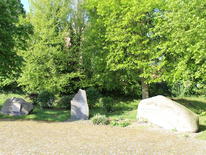 Partnerkommunen Drei Gedenksteine stehen auf einem gepflegten, sonnigen Platz, umgeben von üppigem Grün.