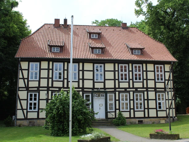 Ein zweigeschossiges Fachwerkgebäude mit roten Dachziegeln und mehreren symmetrisch angeordneten Fenstern.