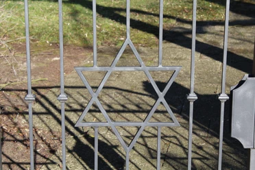 Jüdischer Friedhof Ein schmiedeeiserner Davidstern ziert das Tor eines Friedhofs, Schattenmuster auf dem Boden.