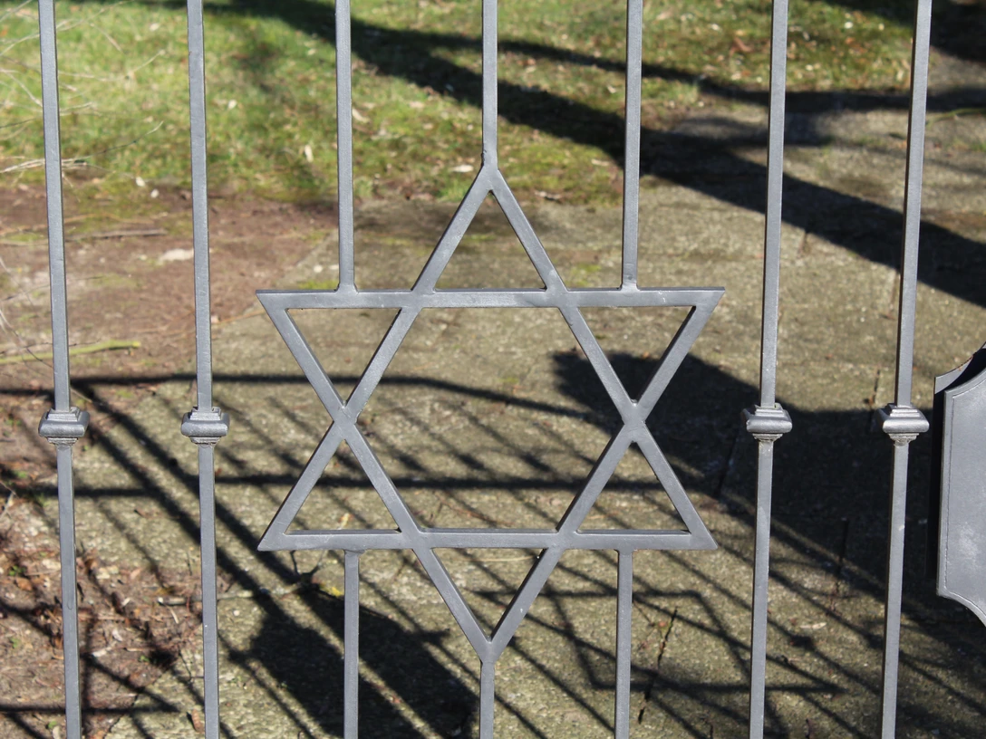 Jüdischer Friedhof Ein schmiedeeiserner Davidstern ziert das Tor eines Friedhofs, Schattenmuster auf dem Boden.