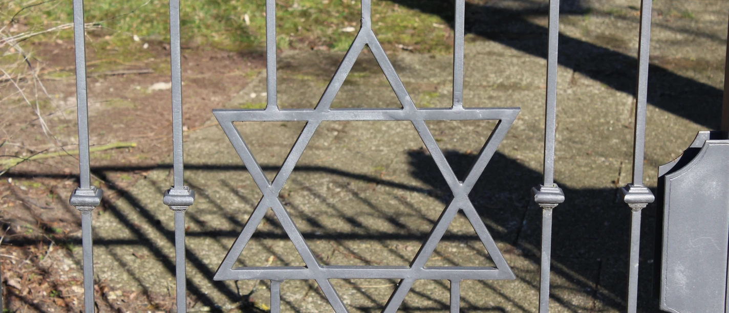Jüdischer Friedhof Ein schmiedeeiserner Davidstern ziert das Tor eines Friedhofs, Schattenmuster auf dem Boden.