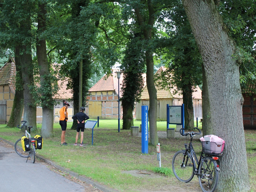 Zwei Radfahrer stehen vor historischen Fachwerkhäusern im Schafstallviertel Hülsen unter grünen Bäumen.