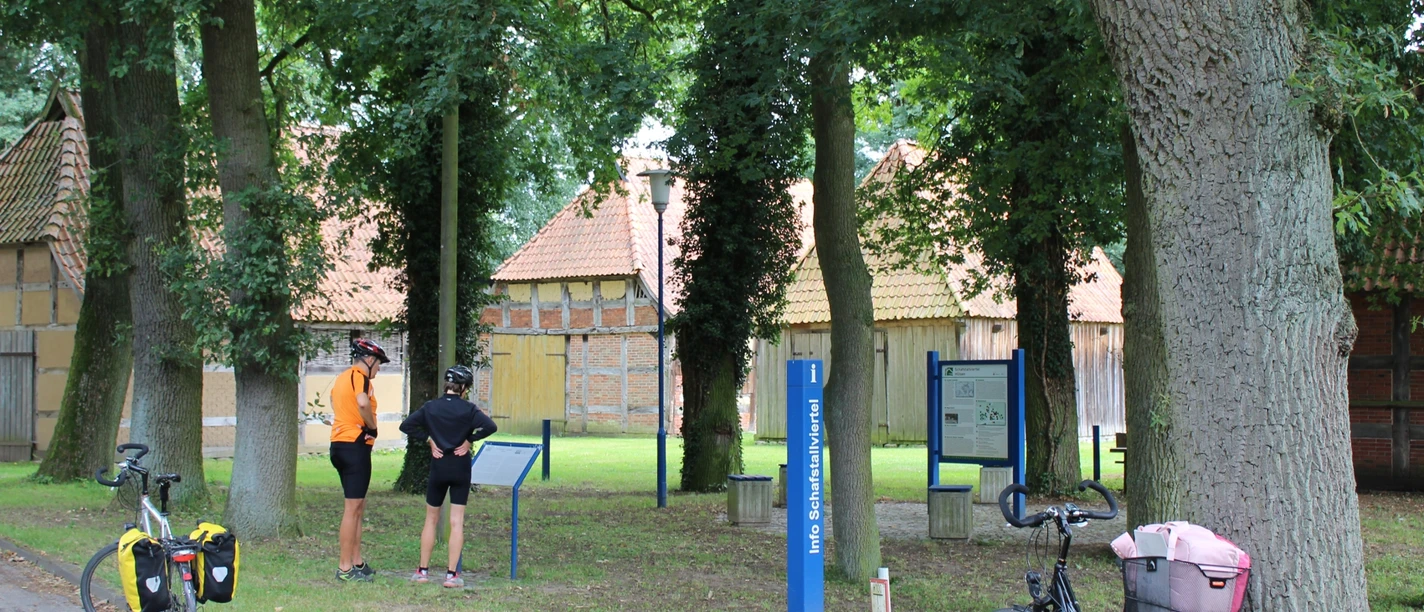 Schafstallviertel Hülsen Zwei Radfahrer stehen vor historischen Fachwerkhäusern im Schafstallviertel Hülsen unter grünen Bäumen.