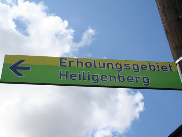 Schild Heiligenberg Grünes Schild mit der Aufschrift "Erholungsgebiet Heiligenberg", blauer Pfeil nach links zeigend.