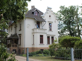 Historische Villa mit verzierten Fassaden und Erkern, eingefasst von üppigem grünen Garten.