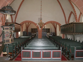 Innenansicht der Ev.-luth. Johannis der Täufer-Kirche mit Holzbänken und einem prunkvollen Kronleuchter.