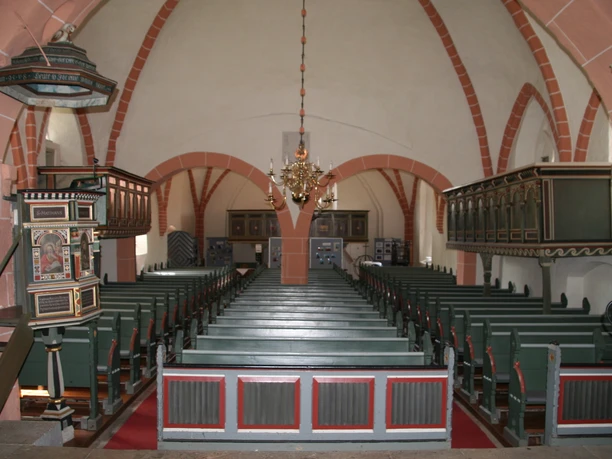 Innenansicht der Ev.-luth. Johannis der Täufer-Kirche mit Holzbänken und einem prunkvollen Kronleuchter.