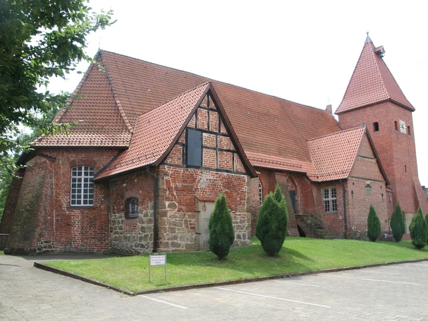 Backsteinkirche aus der Gotik in Drakenburg mit markantem Schnittgiebel und vereinzelt stehenden Bäumen.