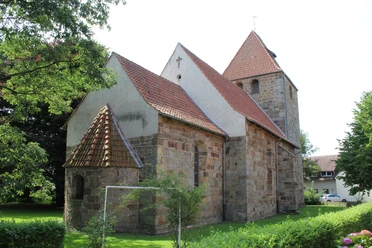 Kirche Buchholz Eine historische Steinkirche mit roten Ziegeldächern, umgeben von Bäumen und grünem Rasen.