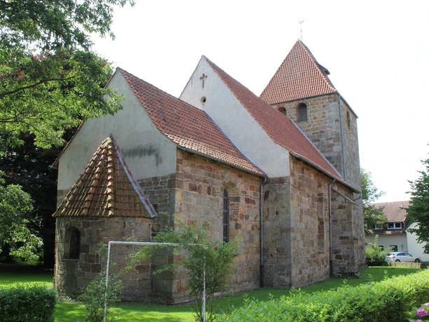 Kirche Buchholz Eine historische Steinkirche mit roten Ziegeldächern, umgeben von Bäumen und grünem Rasen.