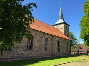 Historische Backsteinkirche in Landesbergen mit spitzem Turm und rotem Dach an einem sonnigen Tag.